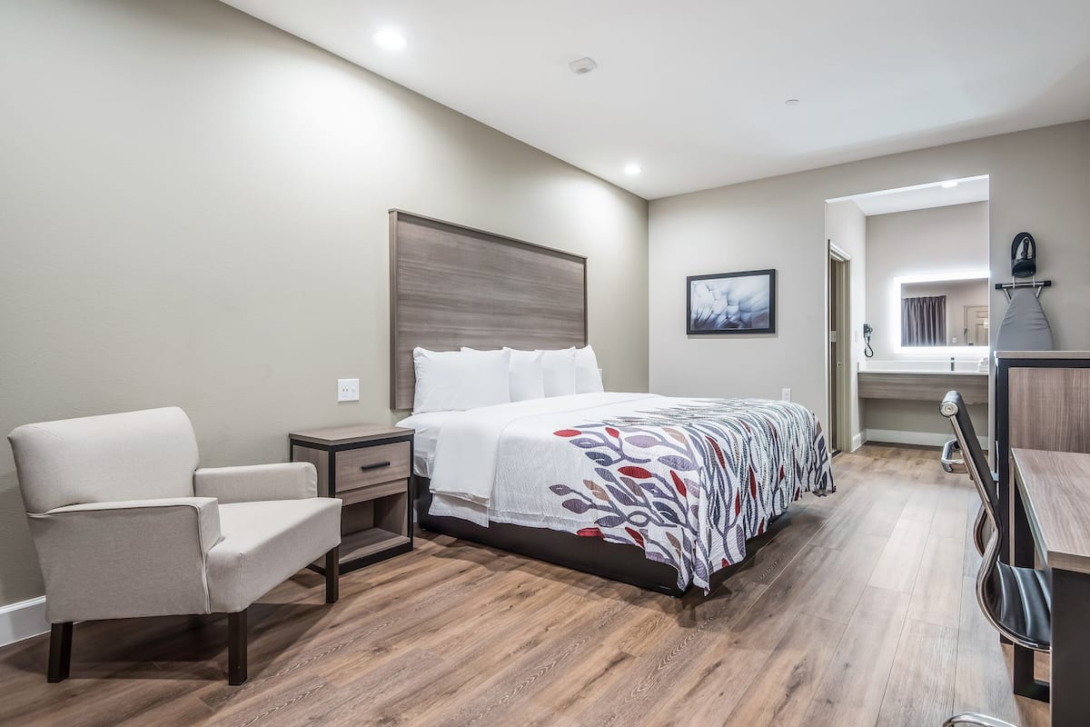 A bedroom with a bed, a chair, a nightstand, and a mirror.