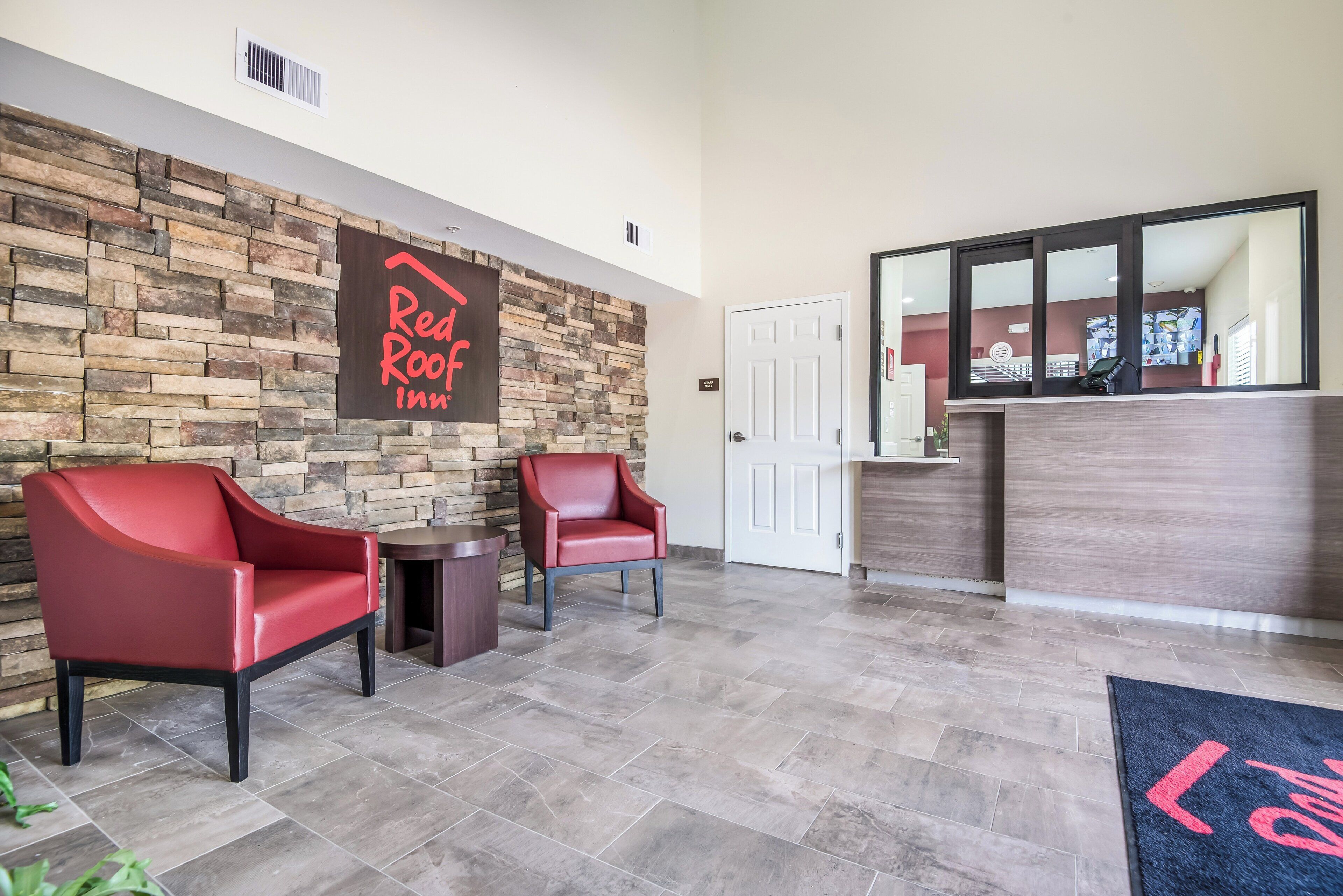A reception area with a stone wall, two red chairs, a reception desk, and a door labeled 'STAFF ONLY'.