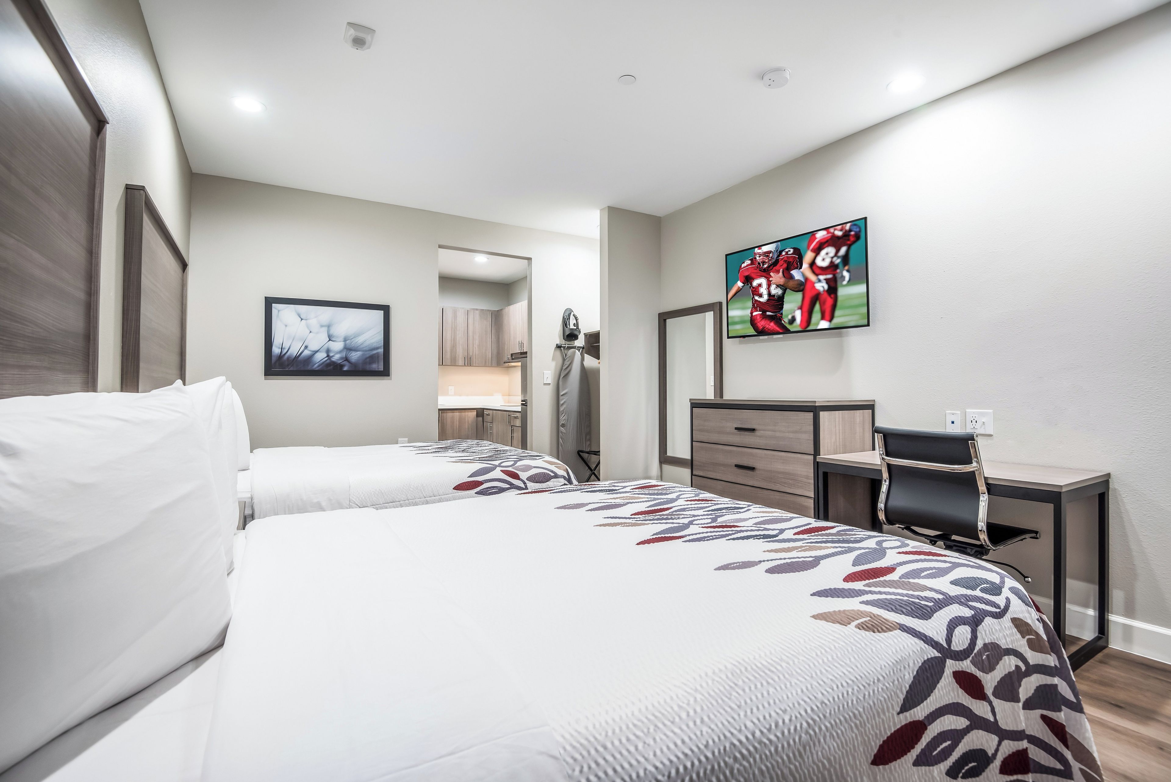 A hotel room with two beds, a desk, a television, and a bathroom visible through an open door.