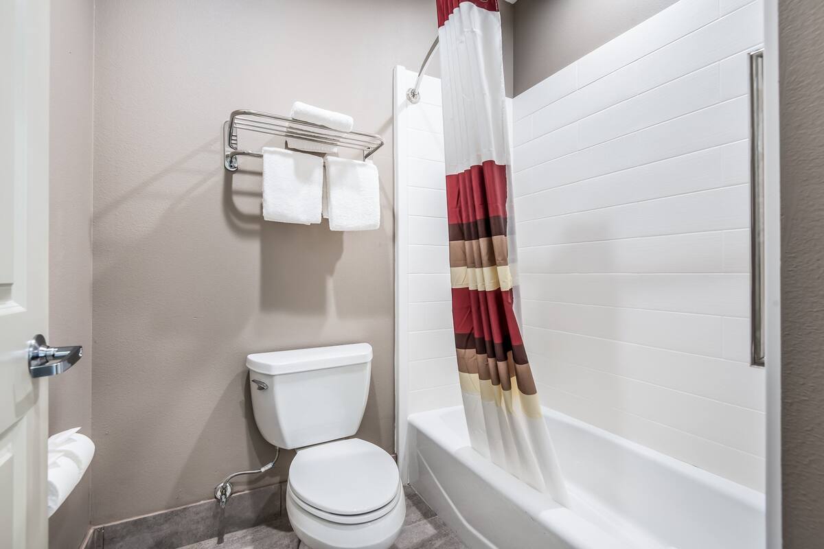A bathroom with a toilet, a towel rack with two towels, a shower curtain, and a bathtub.