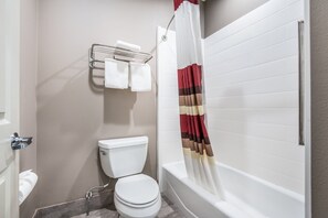 A bathroom with a toilet, a towel rack with two towels, a shower curtain, and a bathtub. - Red Roof Inn Baytown (Baytown)