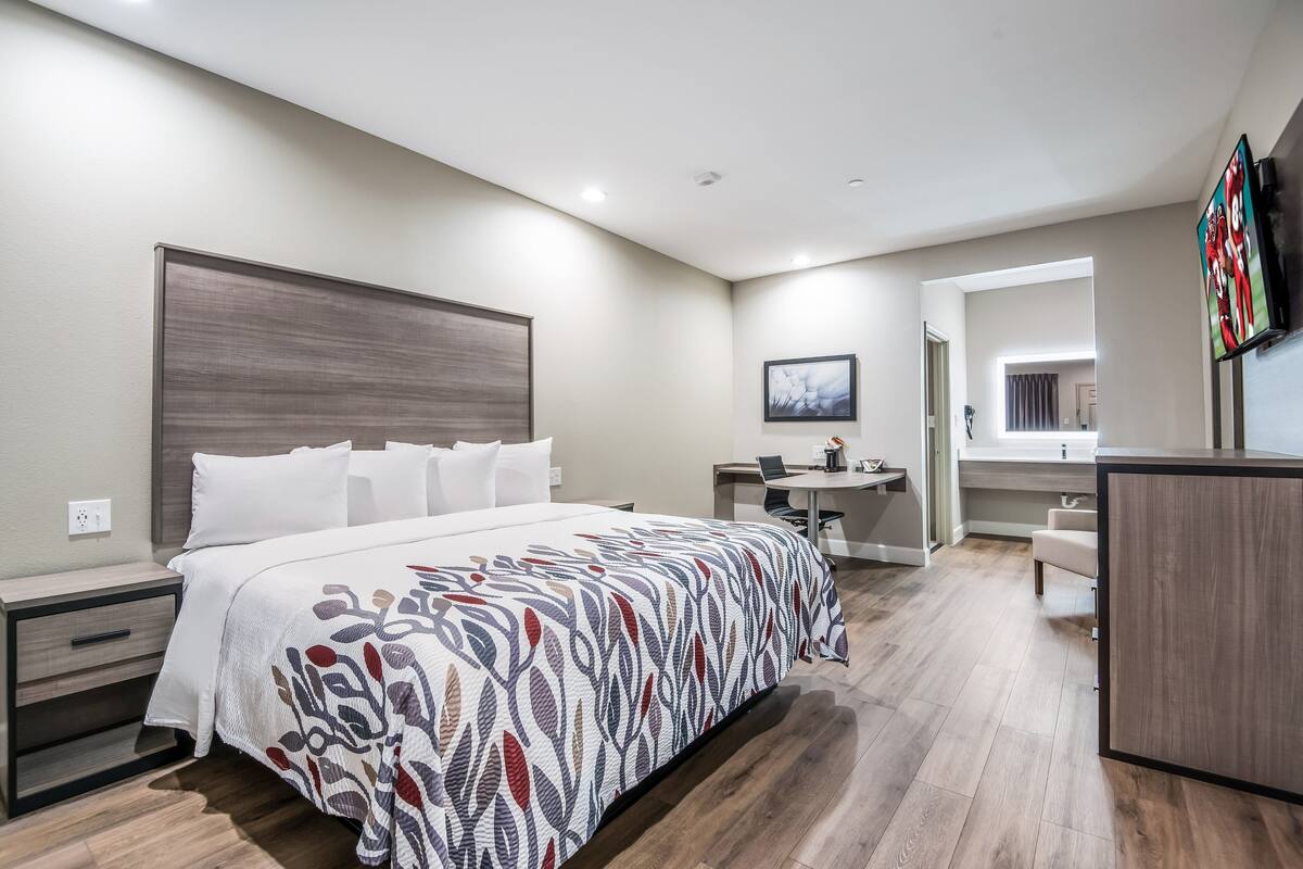 A modern hotel room with a large bed, a desk, and a bathroom visible through an open door.