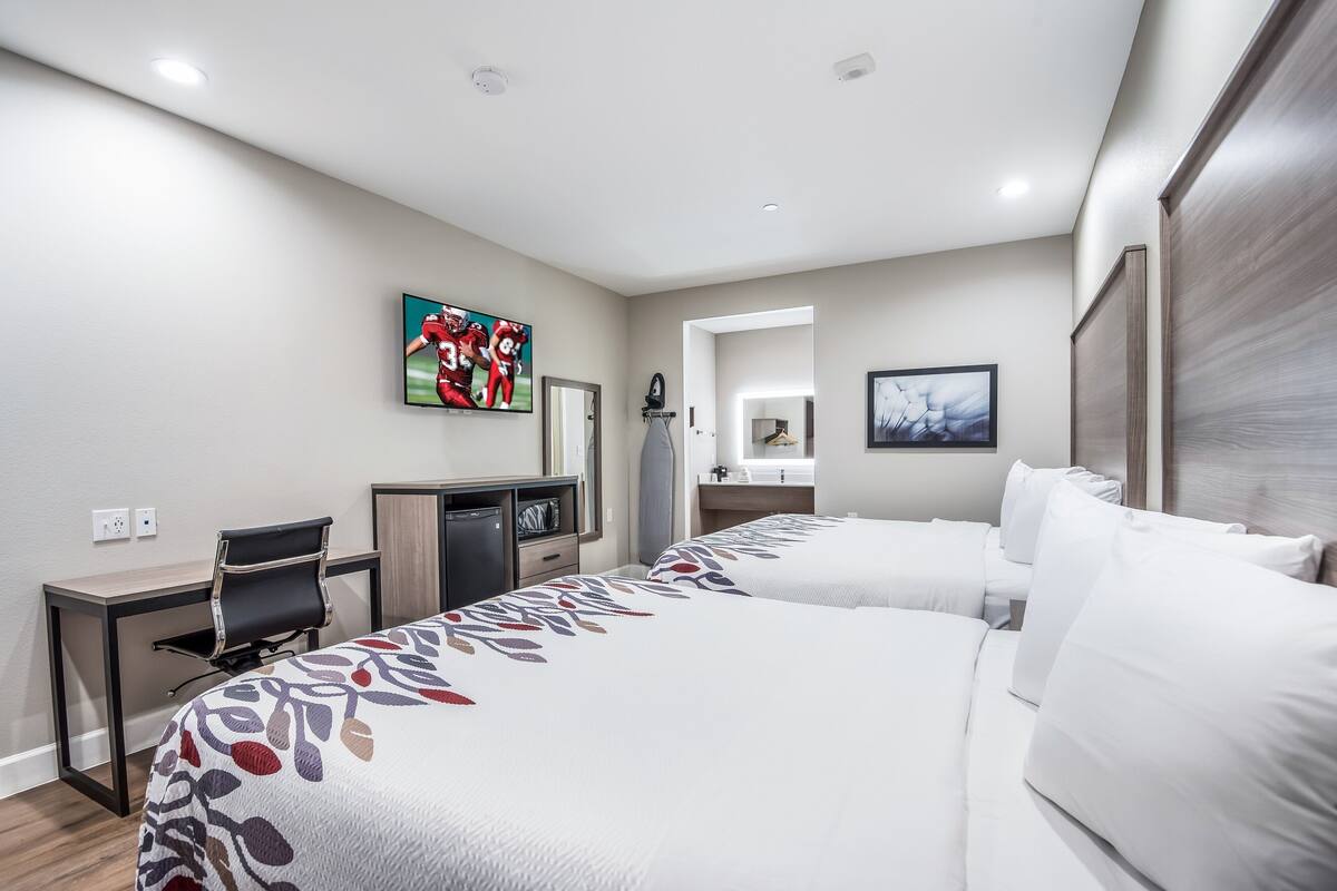 A hotel room with two beds, a desk, a chair, a television, and artwork on the walls.