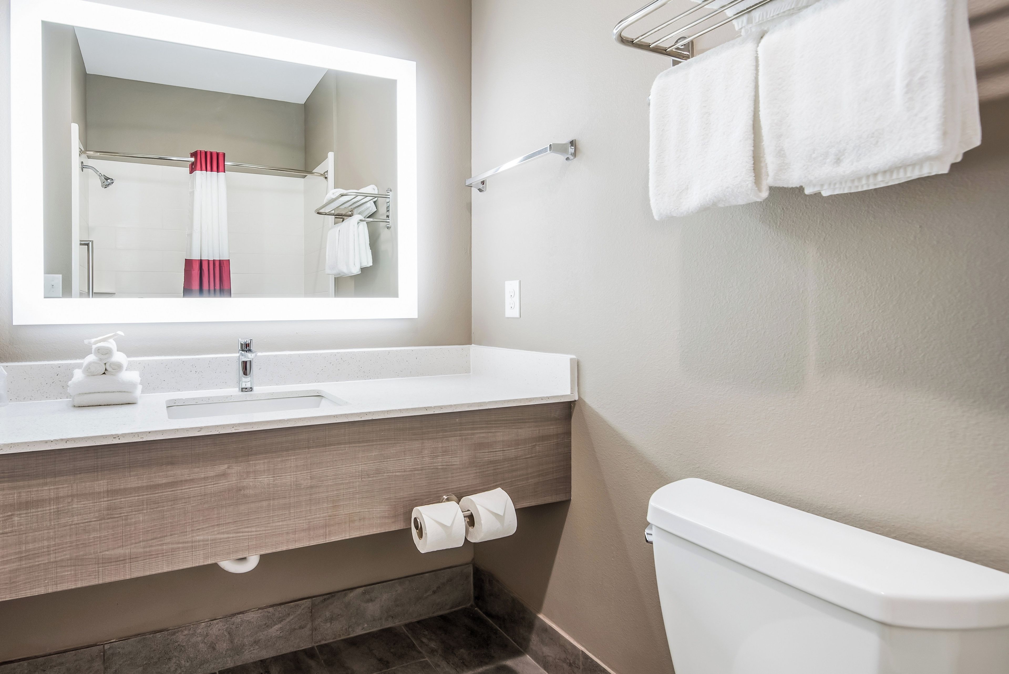 A modern bathroom with a large mirror, a sink, a toilet, and a towel rack.