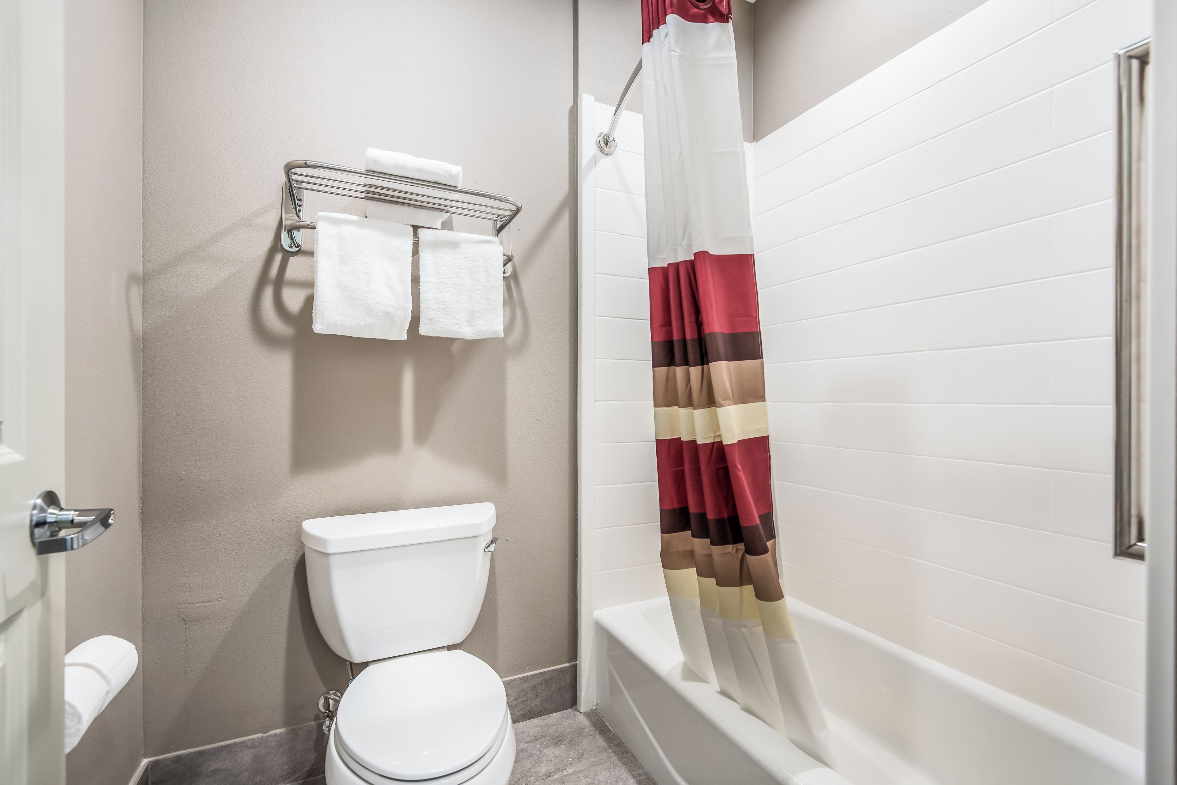 A bathroom with a toilet, a towel rack with two towels, and a shower curtain.