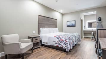 A hotel room with a bed, a chair, a nightstand, a desk, and a bathroom visible through an open door.