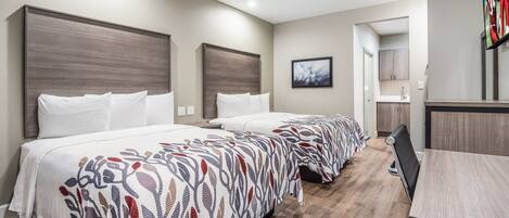 A hotel room with two beds, a desk, and a bathroom visible through an open door.