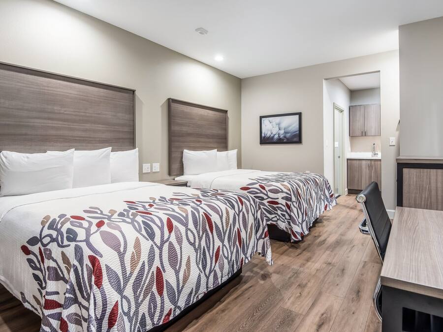 Una habitación de hotel con dos camas, un escritorio y un baño visible a través de una puerta abierta.