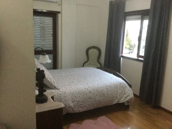 A bedroom with a bed, a chair, a window with curtains, and a door with a window blind.