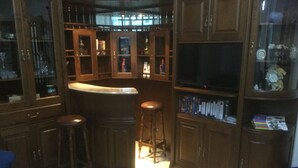 Una zona de bar con taburetes, un televisor y una estantería con libros y objetos decorativos.