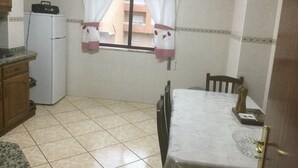 Una pequeña cocina con refrigerador, una mesa y un ventanal con cortinas.