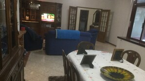 Una sala de estar con un sofá azul, una mesa de comedor con sillas y un televisor al fondo.