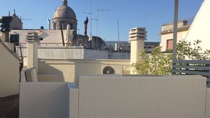 Eine Dachterrasse mit einer Pergola, einem weißen Korbsessel und Blick auf ein historisches Gebäude mit Kuppeln.