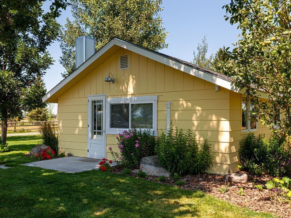 A yellow single-story house with a front porch, a chimney, and a small garden with flowers and shrubs.