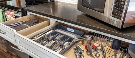 Una cocina con un organizador de cajones que contiene varios utensilios y un microondas.