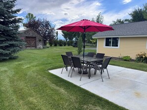 A patio with a table and chairs, a red umbrella, and a well-maintained lawn. - Quite farm house in the country just minutes from town (Bozeman)