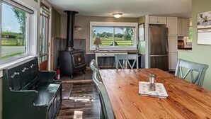 Eine Küche mit Holzofen, einem Esstisch und Blick ins Freie.