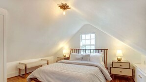 Une chambre avec un plafond en pente, un lit avec un cadre en bois, deux tables de chevet avec des lampes, un banc et une fenêtre.