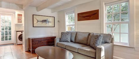 Un salon avec un canapé gris, une table basse ronde en bois et un tableau accroché au mur.