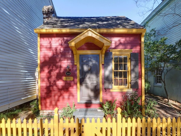 A small, single-story house with a red exterior and yellow trim, a front door, and a mailbox.