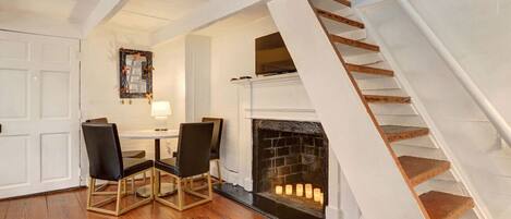 A room with a fireplace, a dining table with chairs, and a staircase.