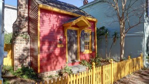 Une maison rouge avec une clôture en bois jaune, une cheminée et un petit porche.