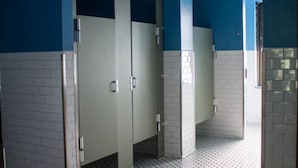 Um banheiro público com paredes azuis, piso de azulejos brancos e corrimão de metal.