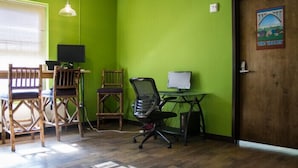 Quarto com parede verde, móveis de madeira, uma escrivaninha com um computador e uma porta com um pôster.