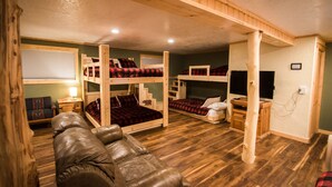 A room with bunk beds, a leather sofa, a small table, and a television. - Wonderful, family friendly 5 Bedroom Cabin in Downtown Red River! (Red River)