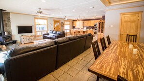 A spacious living room with a large sectional sofa, a wooden dining table, and a kitchen in the background. - Wonderful, family friendly 5 Bedroom Cabin in Downtown Red River! (Red River)