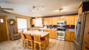 A kitchen with wooden cabinets, a central island with chairs, a refrigerator, and a microwave. - Wonderful, family friendly 5 Bedroom Cabin in Downtown Red River! (Red River)