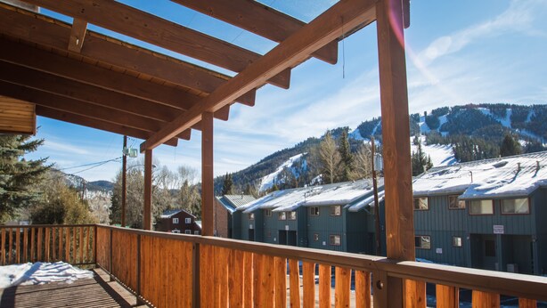 A wooden deck with a view of snow-covered buildings and mountains. - Wonderful, family friendly 5 Bedroom Cabin in Downtown Red River! (Red River)