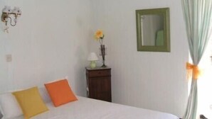Una camera da letto con un letto, due cuscini, un comodino con una lampada, uno specchio e una finestra con tende.