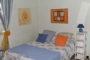 A bedroom with a bed, pillows, a wall art piece, a framed picture, a lamp, and a white storage unit.