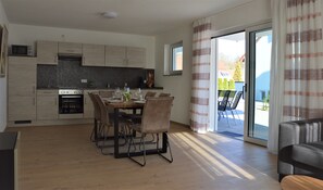 Una cocina moderna con armarios de madera, horno integrado y comedor con una mesa para dos.