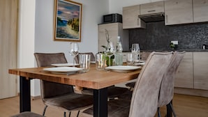 Un comedor con una mesa de madera dispuesta para cuatro personas, rodeada de sillas. Un cuadro de una playa adorna la pared.