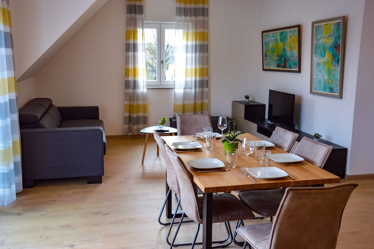 A dining area with a wooden table set for four, a sofa, and a TV in the background.