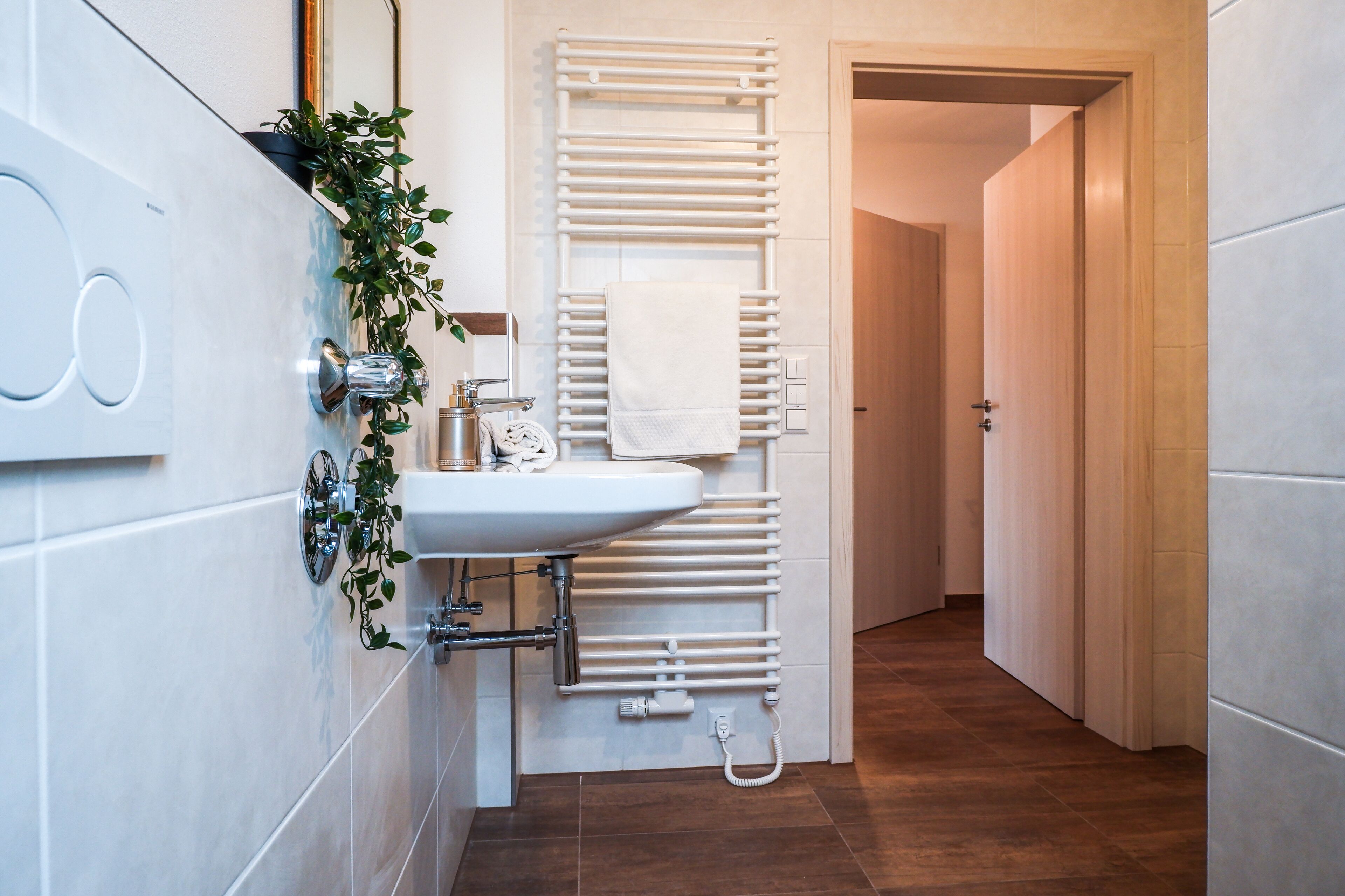 A modern bathroom with a white sink, a towel rack, and a shower.