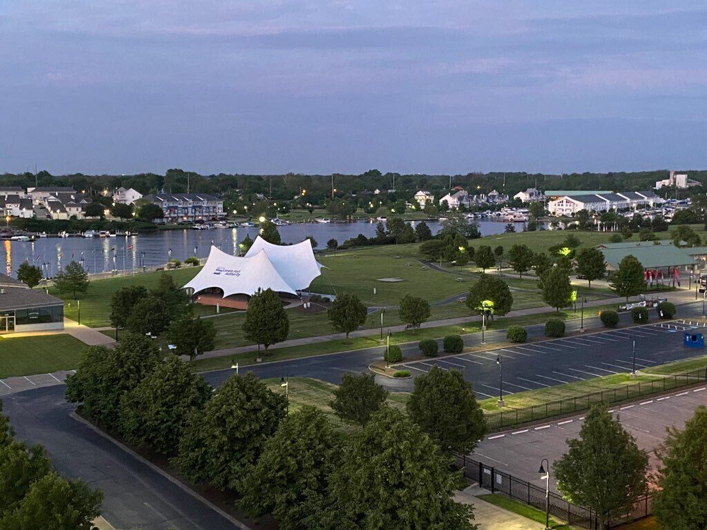 A large white stadium with a unique roof design, surrounded by a parking lot and greenery.