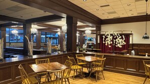 Ein Restaurant mit Holztischen und -stühlen, einer Bar und Blick ins Freie.