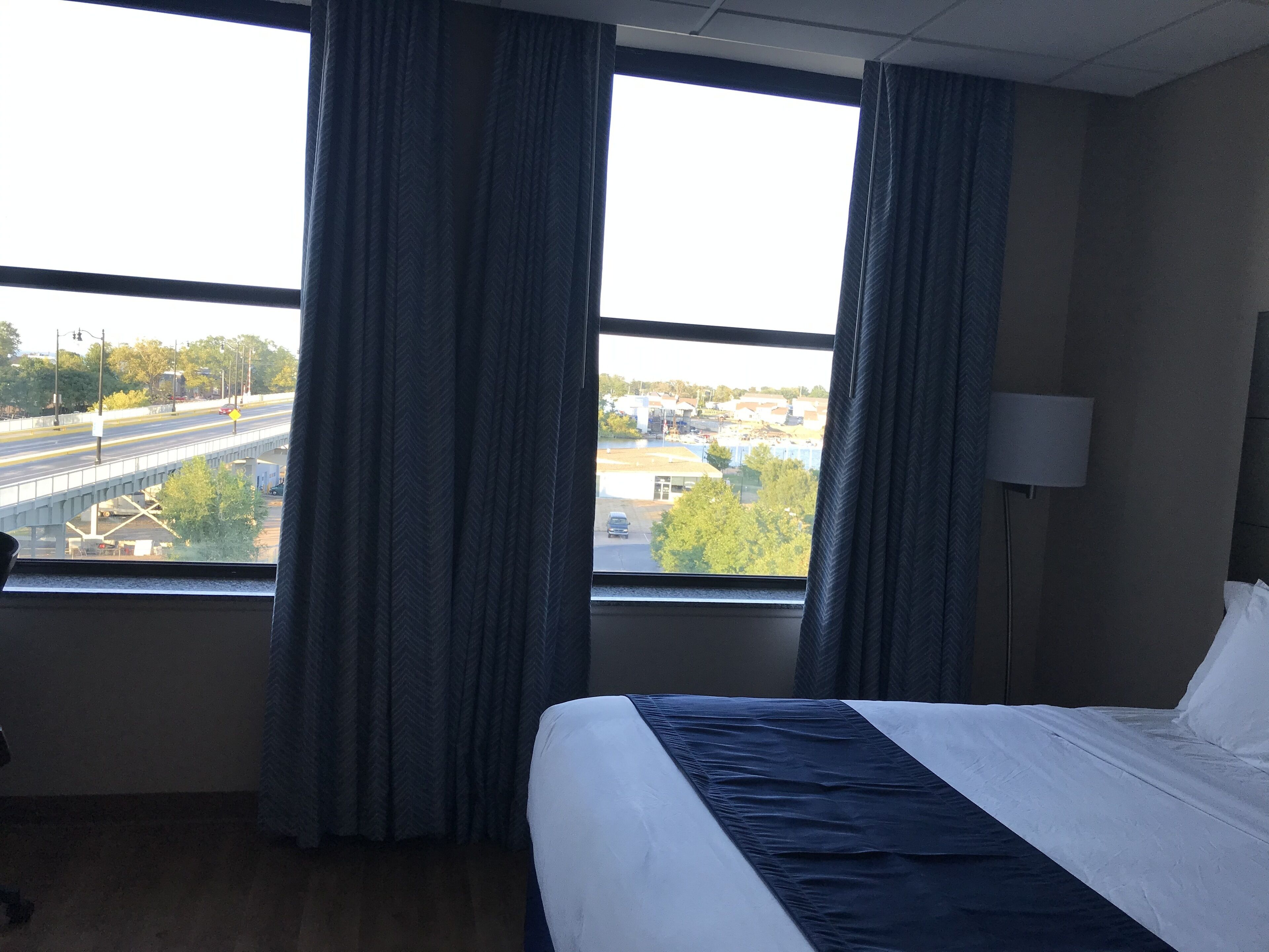 Hotellihuone, jossa on suuri ikkuna, sänky ja lamppu.
