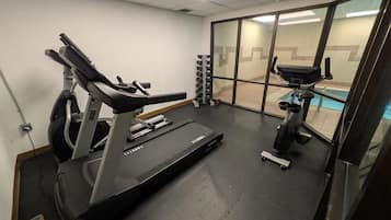 Une salle de sport équipée d’un tapis de course, d’un vélo elliptique et de poids.
