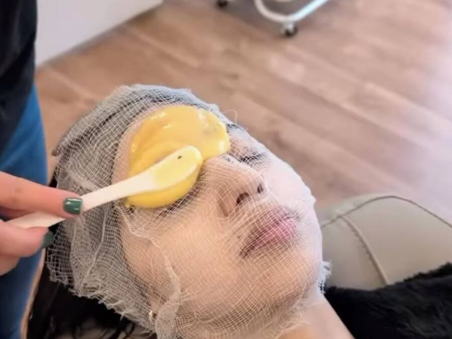 A person receiving a facial treatment with a mask and a bowl of yellow liquid.