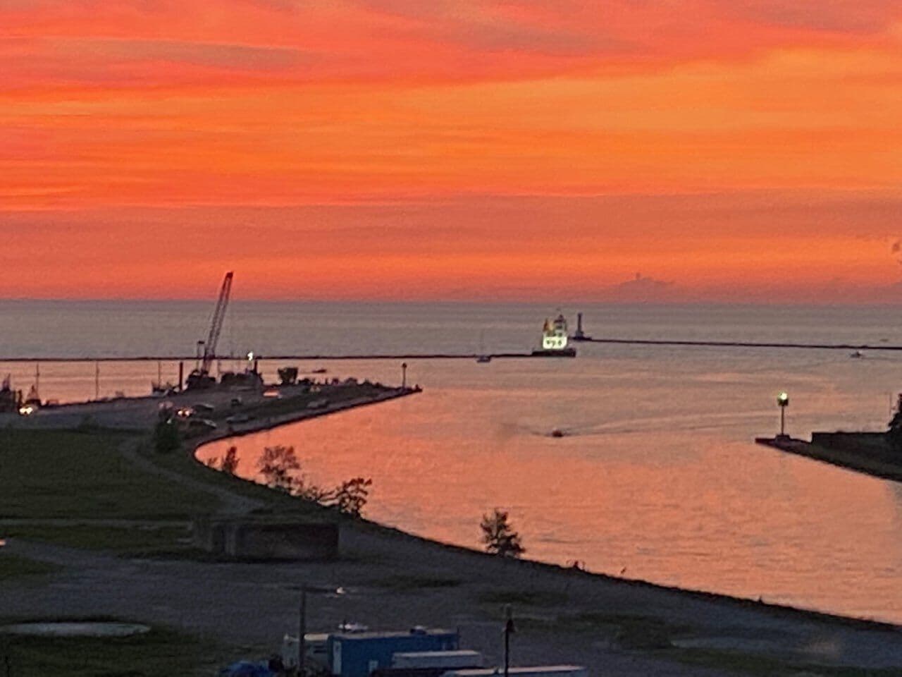 A sunset over a body of water with a ship and industrial structures in the background.