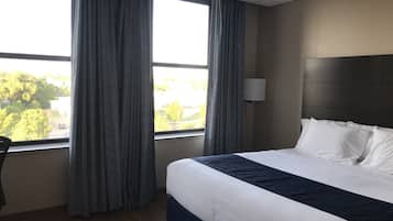 A hotel room with a large bed, a desk, and a window with curtains.