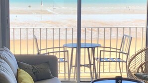 Un balcón con vista a la playa, una mesa redonda y un sofá con cojines.