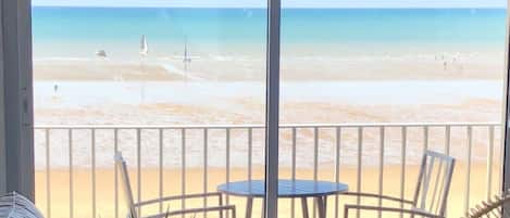 Un balcón con vista a la playa, una mesa redonda y un sofá con cojines.