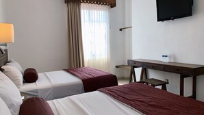 Habitación de hotel con dos camas, un escritorio, una televisión y una ventana con cortinas.
