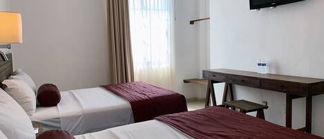 Habitación de hotel con dos camas, un escritorio, una televisión y una ventana con cortinas.