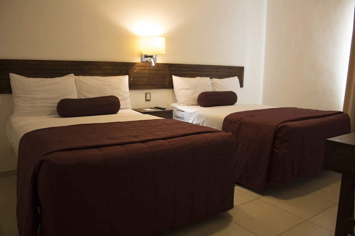 A hotel room with two beds, each with a brown bedspread, a nightstand, and a wall-mounted lamp.